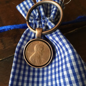 May include: A 1971 US penny coin attached to a blue and white gingham drawstring bag with a copper-colored key ring.