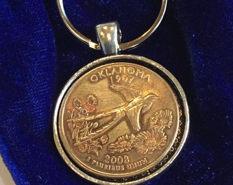 May include: A gold-colored keychain featuring a 2003 Oklahoma state quarter with a depiction of a bird and flowers. The text "Oklahoma 1907" and "E Pluribus Unum" are visible on the coin.