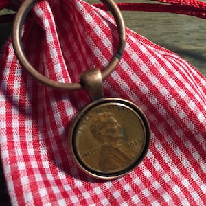 May include: A copper key chain with a 1958 US penny attached. The penny is in a circular frame and has the words "In God We Trust" and "Liberty" on it.