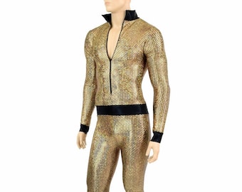 Op de afbeelding: Een gouden jumpsuit met een zwarte rits en zwarte afwerking rond de hals, taille en manchetten. De jumpsuit heeft een geometrisch patroon en wijde pijpen.