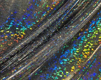 Puede incluir: Primer plano de una tela brillante e iridiscente. El material es gris oscuro o negro, con un sutil patrón de cuadrícula. Dispersos por la superficie hay motas vibrantes y coloridas que reflejan la luz, creando un efecto holográfico. La tela está drapeada, mostrando pliegues y textura.