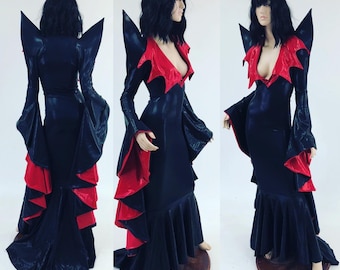 May include: A black and red gothic-style dress with a plunging neckline and flared sleeves. The dress features a high collar and a ruffled hem. The dress is displayed on a mannequin, showcasing its design and fit. The dress is made of a shiny material.
