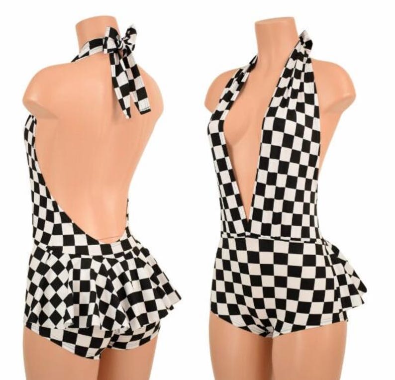 May include: A black and white checkered halter romper featuring a deep V-neckline, a tie-back neck closure, and a flared skirt overlay attached to the shorts. The garment displays a consistent geometric checkerboard pattern throughout the entire piece.
