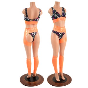May include: A two-piece outfit with a black and white patterned top and matching shorts. The top has a scoop neck and the shorts have a high waist and a cut-out detail on the back. The outfit is accented with bright orange trim and leg warmers.