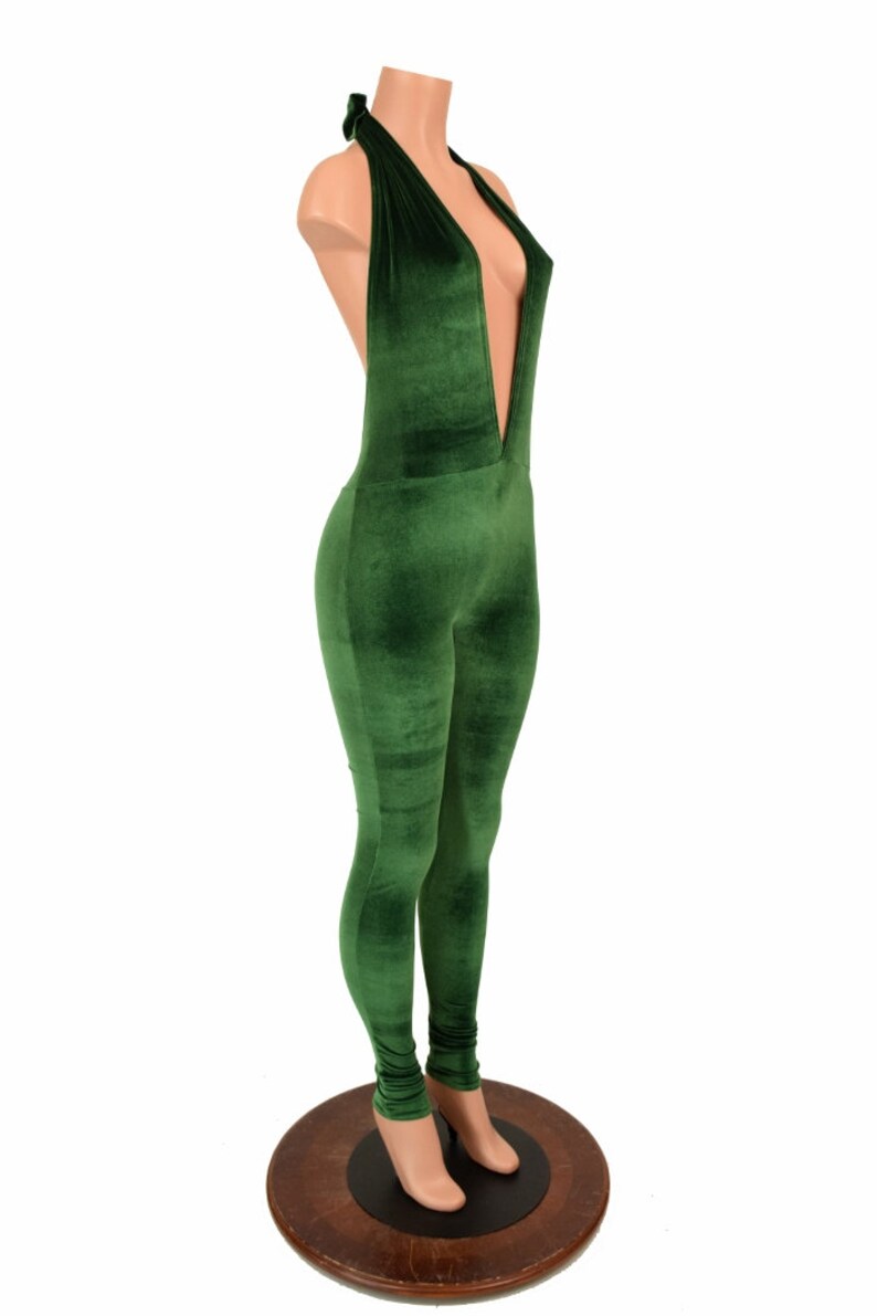 May include: A green velvet jumpsuit with a plunging neckline and halter tie. The one-piece garment is form-fitting, with long sleeves and legs. The jumpsuit is displayed on a mannequin.