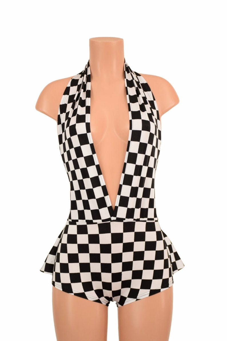 May include: A black and white checkered bodysuit featuring a deep plunging halter neckline and a flared peplum waist detail. The garment is displayed on a mannequin and showcases a consistent geometric square pattern throughout the entire piece.
