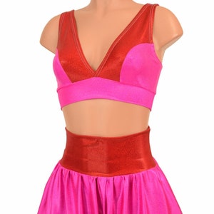 May include: A pink and red two-piece costume with a halter top and harem pants. The top has a V-neckline and a red band around the waist. The pants have a wide leg and a red band around the waist.