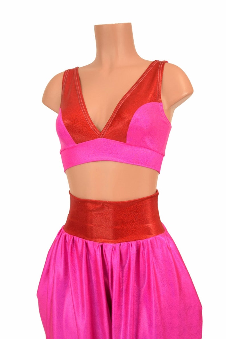May include: A pink and red two-piece costume with a halter top and harem pants. The top has a V-neckline and a red band around the waist. The pants have a wide leg and a red band around the waist.