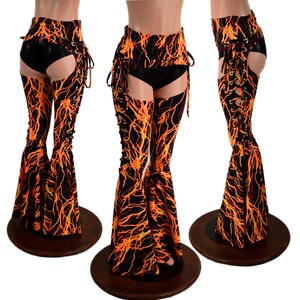 May include: Three pairs of black and orange patterned flared pants with lace-up detailing. The pants have a high waist and cut-out sections. The orange pattern resembles lightning or flames. The pants are displayed on mannequins.
