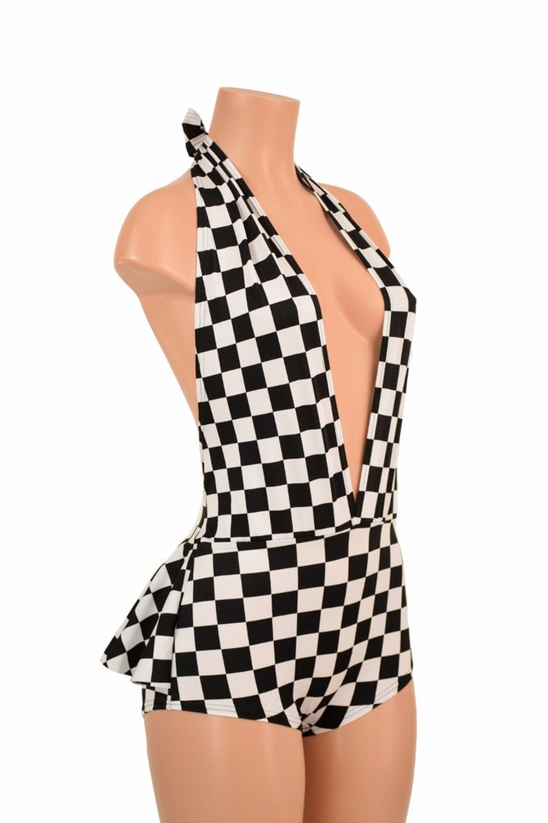 May include: A black and white checkered halter bodysuit featuring a deep plunging neckline and a ruffled peplum detail at the waist. The garment is displayed on a mannequin, showcasing the repeating square pattern across the entire piece.