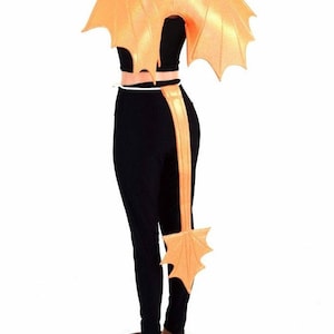 May include: A peach-colored dragon tail and wings costume. The tail is long and has a pointed tip with a fan of feathers. The wings are large and have a similar feather design. The costume is worn on a mannequin.