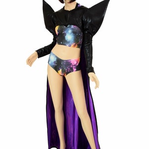 May include: A mannequin displays a futuristic costume. The outfit includes a black, long-sleeved top with large shoulder accents, a matching cape with a purple lining, and a crop top and shorts set with a galaxy print. The mannequin has a dark bob.