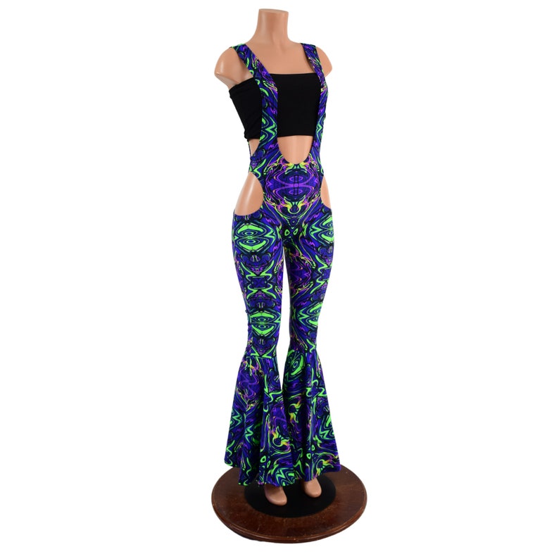May include: Purple and green patterned bell bottom pants with a cutout on the side and suspenders. The pants are on a mannequin.