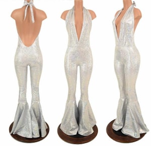 May include: A silver holographic jumpsuit featuring a deep V-neckline, a halter-style neck tie, and flared pant legs. The garment is shown from three different angles, displaying the back with a tie closure, the front view, and a side profile.