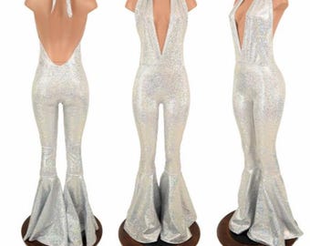 May include: A silver holographic jumpsuit featuring a deep V-neckline, a halter-style neck tie, and flared pant legs. The garment is shown from three different angles, displaying the back with a tie closure, the front view, and a side profile.