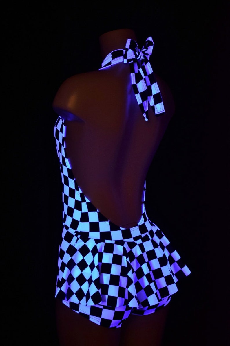 May include: A black and white checkered halter top with a flared peplum waist and a tie-neck closure. The garment is illuminated under ultraviolet light, causing the white squares to glow brightly against the dark background of the fabric.