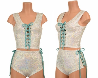 May include: A two-piece outfit in a silver iridescent fabric with teal lace-up details. The top is a cropped tank top with a V-neck and the shorts are high-waisted with side ties.