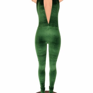 May include: A green velvet jumpsuit with a halter neckline and a plunging V-neck. The jumpsuit is displayed on a mannequin and has a form-fitting silhouette. The legs are long and fitted, with a slight gathering at the ankles.