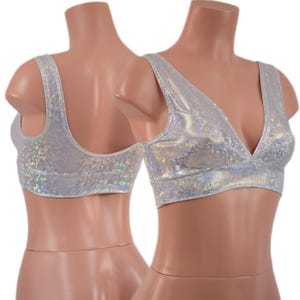 May include: Two silver, shimmering crop tops with a V-neck design are displayed on mannequins. The tops have wide straps and a textured, iridescent finish, reflecting light. The tops are designed for dance or festival wear.