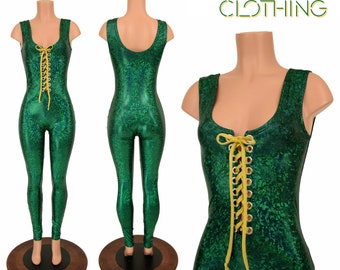 May include: Green sparkly jumpsuit with a yellow lace-up detail in the front. The jumpsuit has a scoop neck and sleeveless design. The model is wearing the jumpsuit on a wooden platform.