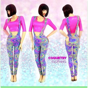 May include: A pink crop top with a scoop neck and short sleeves is worn over a pair of colorful swirl print pants with suspenders. The pants have a low rise and a wide leg. The model is wearing the outfit with a confident pose. The text "COQUETRY CLOTHING" is visible in the image.