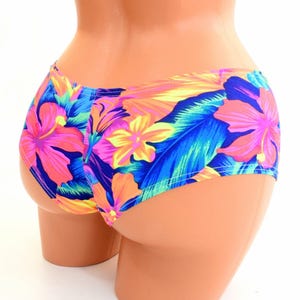 May include: Floral print bikini bottoms with a bright orange, pink, blue, and yellow color scheme. The bottoms are on a mannequin.