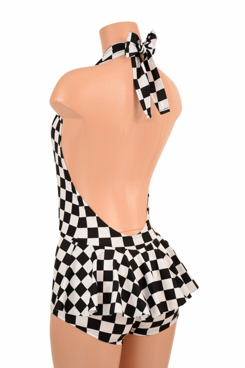 May include: A black and white checkered halter top featuring a deep open back design with a tie closure at the neck and a flared peplum hem. The garment is displayed on a mannequin, showcasing the repeating square pattern across the entire piece.