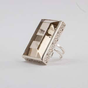 May include: A silver ring with a rectangular, clear, smoky quartz stone set in a filigree design.