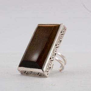 May include: A silver ring with a rectangular brown tiger's eye stone. The ring has a decorative, intricate design around the stone.
