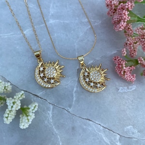 May include: Two gold necklaces with a sun and moon pendant. Each pendant is adorned with clear cubic zirconia stones.