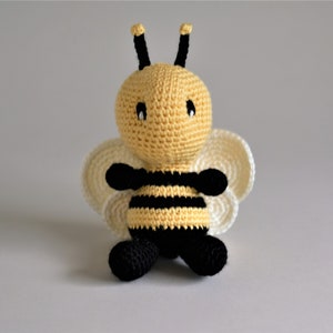 May include: A crocheted bee toy with black and yellow stripes, white wings, and black eyes.