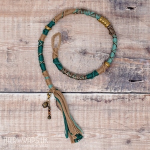 Peut inclure: Un enrouleur de cheveux vert et marron avec un pompon et un charme. L'enrouleur est fait de plusieurs brins de cordon et a une section perlée.