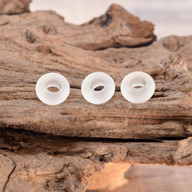 May include: Three white frosted glass tunnels, each with a circular hole in the centre, are arranged in a row on a piece of weathered wood.