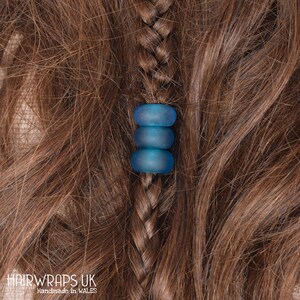 May include: Three blue glass beads strung together on a braid of brown hair. The beads are translucent and have a slightly frosted finish.