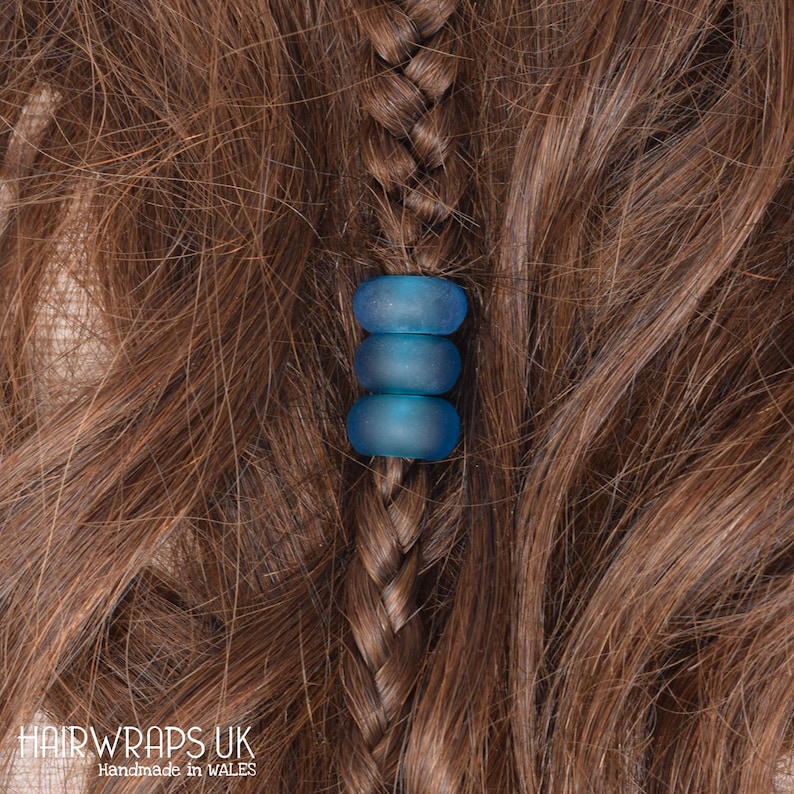 May include: Three blue glass beads strung together on a braid of brown hair. The beads are translucent and have a slightly frosted finish.