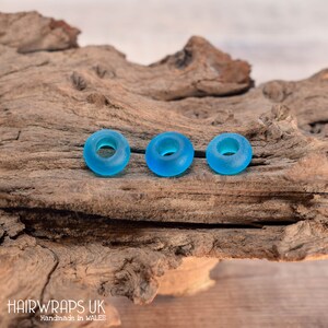 May include: Three turquoise blue glass hair tie beads on a wooden surface.