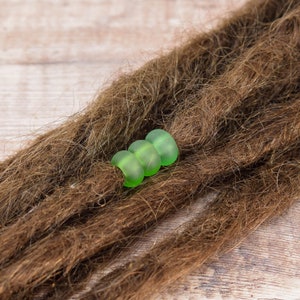 May include: Three green glass beads strung together on brown dreadlocks.