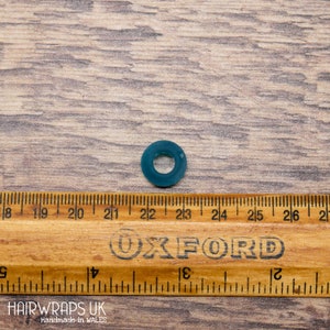 May include: A teal blue rubber hair tie, measured against a ruler, with the brand name "Oxford" printed on the ruler.