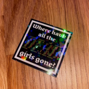 May include: A square sticker with a black background and white border. The text "Where have all the girls gone?" is written in white. The word "girls" is in a glitch effect. The sticker has a holographic, iridescent finish.