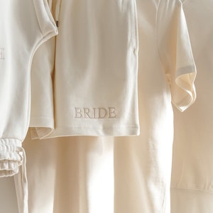 May include: A white cotton sweatshirt and matching shorts with the word "BRIDE" embroidered on the shorts.