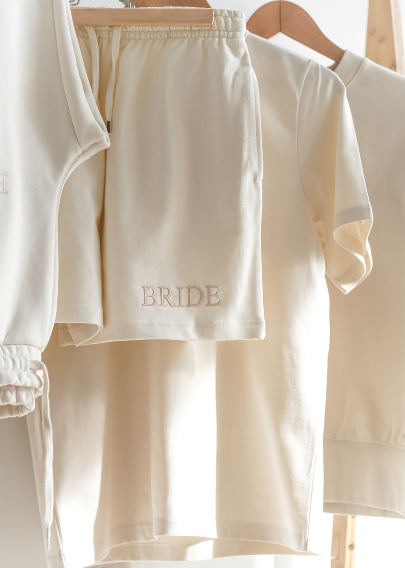 May include: A white cotton sweatshirt and matching shorts with the word "BRIDE" embroidered on the shorts.