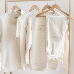 May include: A cream-coloured sweatshirt and sweatpants set with the word "Wife" embroidered on the sweatshirt and "Wife" embroidered on the sweatpants.