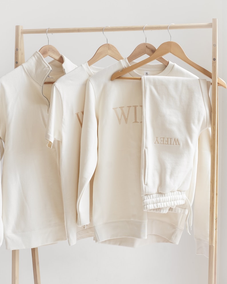 May include: A cream-coloured sweatshirt and sweatpants set with the word "Wife" embroidered on the sweatshirt and "Wife" embroidered on the sweatpants.