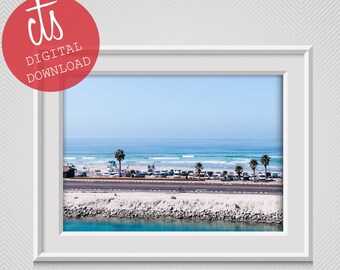 May include: A framed digital print of a coastal scene. The image features a beach, ocean, road, and palm trees under a clear blue sky. The print is in a white frame, with the text "cts DIGITAL DOWNLOAD" in a red circle.