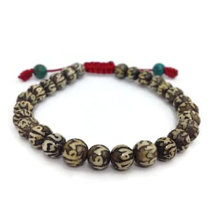May include: A brown and white prayer bead bracelet with a red and turquoise tassel. The beads are engraved with Tibetan characters.