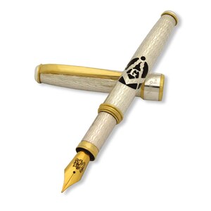 May include: A silver and gold fountain pen with a black and white Masonic symbol engraved on the barrel. The pen has a gold trim and a fine nib.