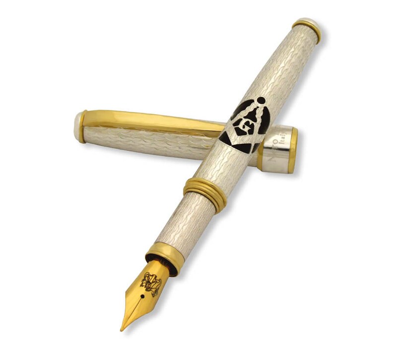 May include: A silver and gold fountain pen with a black and white Masonic symbol engraved on the barrel. The pen has a gold trim and a fine nib.