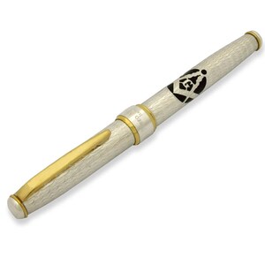 May include: A silver and gold pen with a textured finish. The pen has a gold band with the word "ORO" engraved on it. The pen also features a black and white Masonic symbol.