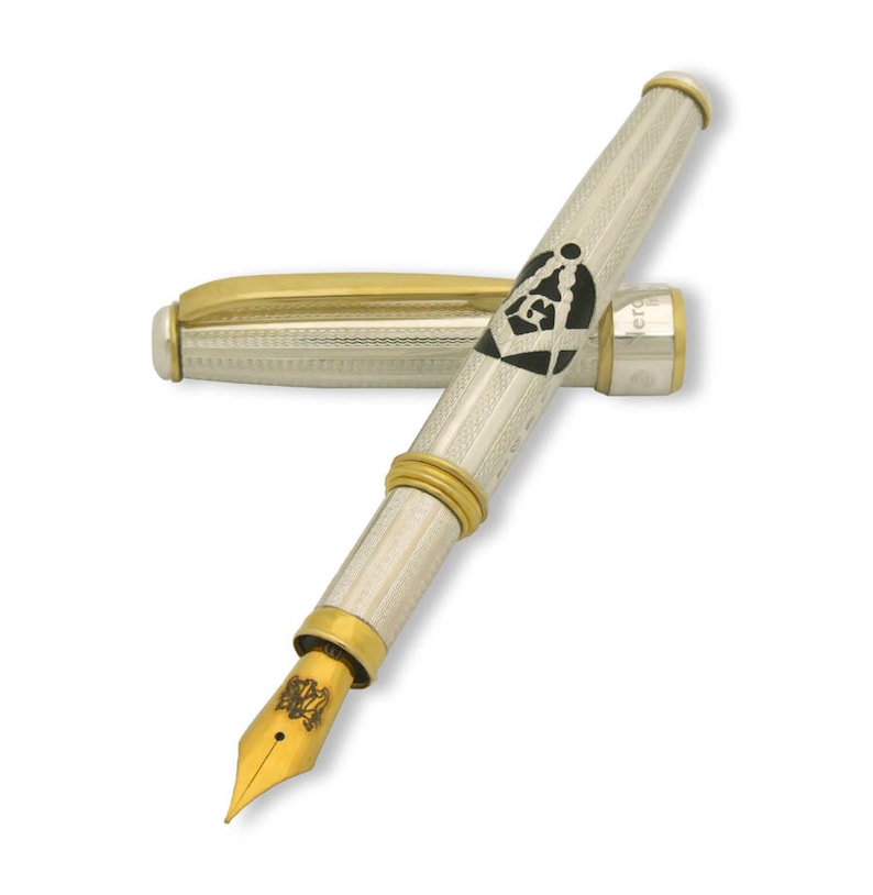 May include: A silver and gold fountain pen with a black and white Masonic symbol on the barrel. The pen has a gold nib and a silver cap.
