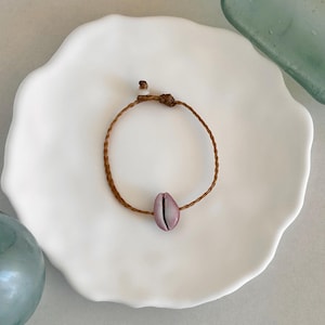 May include: A brown braided cord bracelet with a pink seashell charm.